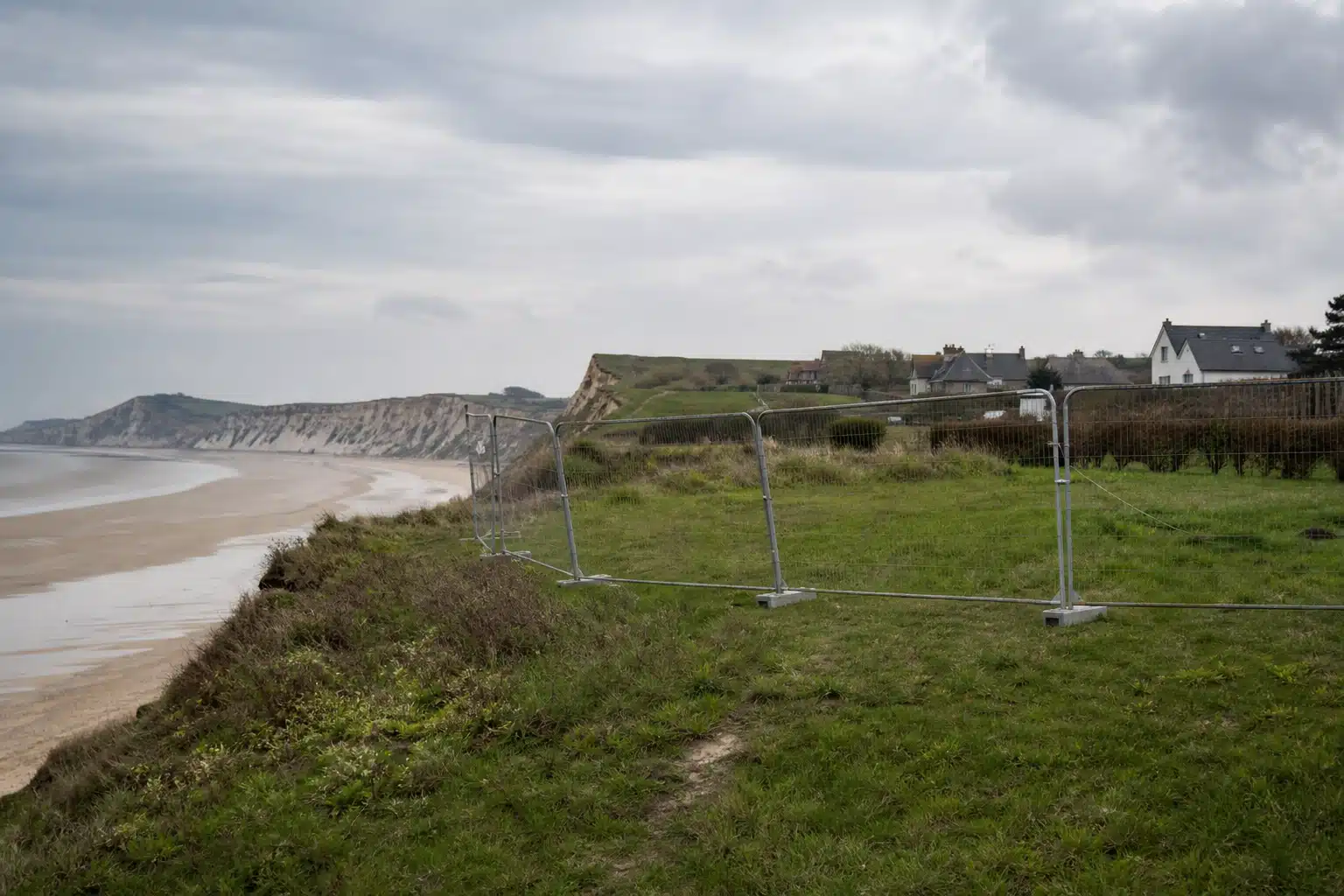 falaise herbeuse bordée d'une clôture temporaire et plage